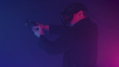 Close Up of Young Man Using Virtual Reality Glasses Holding and Using Joysticks Controllers as a Gun to Play Shooting Game at the Abstract Neon Lighting Background.