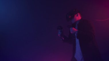 Young Man Wearing Virtual Reality Headset, Boxes, Moves hands, Traines kicking, Holding Controllers Joysticks Standing at Neon Lighting Colors Futurictic Background.