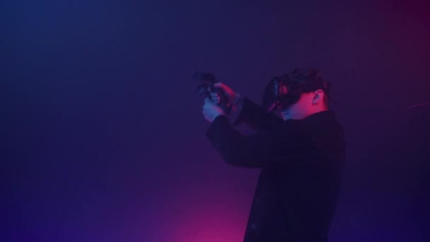 Jovem Gamer em realidade virtual Headset Jogar jogo de tiro on-line, Usando controladores para atirar no fundo de iluminação de néon cibernético. Fechar . — Vídeo de Stock