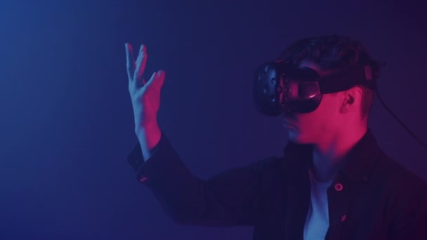 Крупним планом портрет враженого хлопця в окулярах віртуальної реальності Дивлячись на його руку, тримаючи віртуальний об'єкт, кажучи WoW стоячи в кімнаті з неоновим освітленням кольори фон . — стокове відео