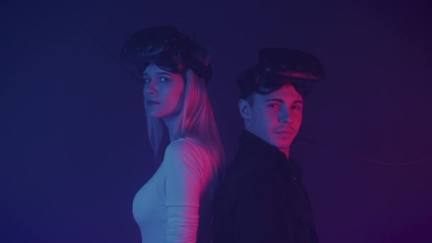 Close Up Portrait of two Gamers Young Man and Girl Standing at the Cyber Neon Lighting Background with Virtual Reality Glasses at their Head, Looking to Camera. — 图库视频影像