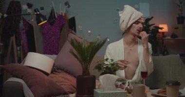 Evde travesti bir erkek, koltukta oturup, oje sürmek için el sıkışıyor ve üflüyor. Rahatlamış adam güzellik prosedürleri yapıyor ve şarap içiyor..