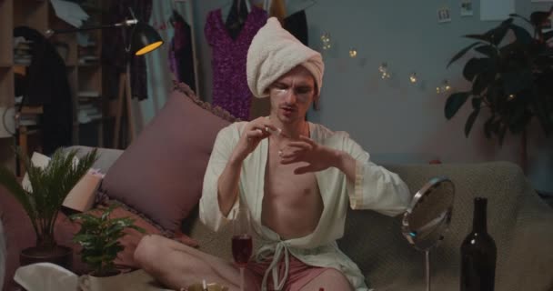 Front view of man transgender in after bath robe painting his nails and getting upset of result. Young trans man sitting on sofa and doing beauty procedures while preparing to party. — Stockvideo