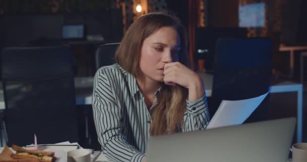 Вид изможденной офисной работницы, читающей документы и сонной. Молодая деловая женщина работает допоздна в ночном офисе и закрывает глаза, чувствуя усталость. . — стоковое видео