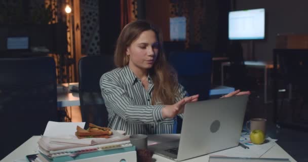 Verveelde zakenvrouw doet yoga-oefeningen en ademt diep om te kalmeren terwijl ze 's avonds laat werkt. Gestresst meisje sluiten van haar laptop terwijl zitten op lege werkplek. — Stockvideo