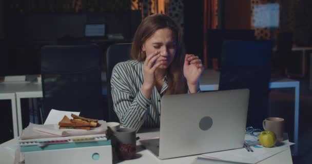 Молода стресова жінка виглядає втомленою і вигорає, працюючи на ноутбуці в нічному офісі. Виснажена дівчина панікує через труднощі і тиск, сидячи за столом . — стокове відео