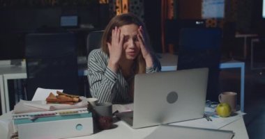 Stresli genç bir kadın dizüstü bilgisayar kullanırken sorun yaşadığı için üzgün görünüyor. Kişisel bilgisayarla çalışan depresyonda bir kız ve gece ofisindeki hatadan dolayı üzgün..