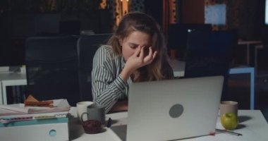 Masada otururken konsantre olmak için alnına masaj yapan genç bir iş kadını. Bitkin düşmüş kadın ofis çalışanı boş gece ofisindeki mali raporunu bitirmek için bilgisayarını kullanıyor..