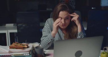 Gece geç saatlere kadar boş ofisinde laptopuyla çalışan çok çalışan bir kadın. Yorgun görünen, uzun saatler çalışırken yüzüne dokunan ve dokunan genç bir kadın..