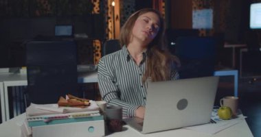 Ofisteki kadın ofis çalışanının dizüstü bilgisayarını ve boyun bükme hareketlerini ön planda görüyoruz. Masada oturup saatlerce çalışırken bilgisayarın ekranına bakmaktan yorgun bir kız.