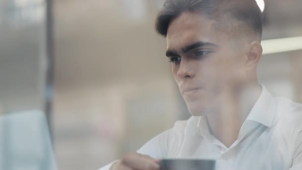 Joven hombre de negocios enojado sentado en la mesa con el ordenador portátil y beber café frío. Reflejo de ventana. Trabajo duro, adicto al trabajo, bancarrota, fracaso, pérdida del concepto de negocio . — Vídeo de stock