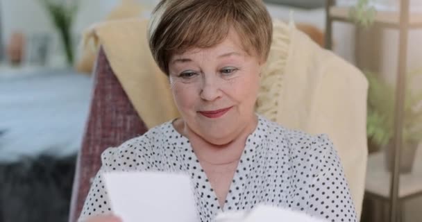 Primer plano de la abuela alegre mirando fotos de la familia mientras está sentado en la silla. Mujer jubilada de buen aspecto emocional sosteniendo viejas fotografías y teniendo nostalgia. Concepto de recuerdos . — Vídeo de stock