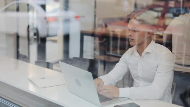 Cansado jovem empresário sentado em uma mesa em um café trabalhando em um laptop. Freelance, comunicação, TI, conceito de empresário cansado — Vídeo de Stock