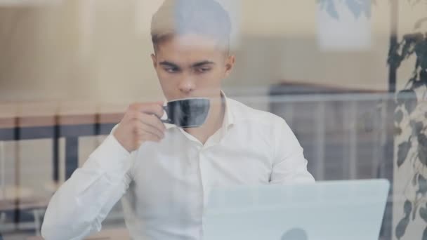 Joven hombre de negocios sentado en la mesa con portátil y beber café. Atractivo manager masculino en camisa blanca con trabajo serio — Vídeos de Stock