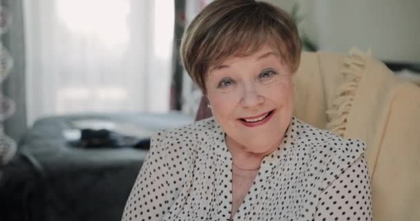 Close up view of cheerful female pensioner sitting on chair at her apartment. Portrait ofgood looking old lady smiling while looking to camera. Concept of peole and positive emotions. — Stock Video