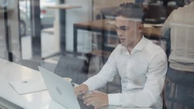 Mutlu genç iş bir dizüstü bilgisayarda çalışan bir kafede bir masada oturuyor. Evet jest, gösterilen laptop arıyorum kazanan zafer, zevk başarı, web üzerinde iyi haber kutlama yaptı