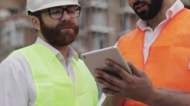 Şantiye yakın tablet kullanarak mimar elleri yakın. Kurucu ve mimar adam modern iş merkezinin inşaat planını tartışıyor.