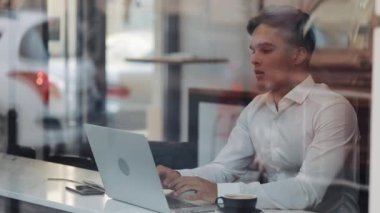 Genç çekici iş adamı dizüstü bilgisayarla ofis işini bitirirken, iş bitince rahatlıyor. Ellerini uzatır, bütün görevlerini tamamlar, kafede oturur.