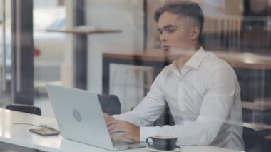 Genç çekici iş adamı dizüstü bilgisayarla ofis işini bitirirken, iş bitince rahatlıyor. Ellerini uzatır, bütün görevlerini tamamlar, kafede oturur.