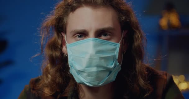 Close up view of millenial man in protective mask on face looking to camera. Portrait of young guy staying at home on quarantine. Concept of safety life, coronavirus, virus protection. — Stock Video