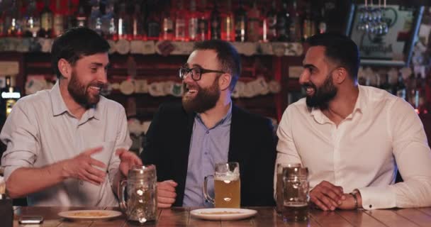 Londres Royaume-Uni - 14 avril 2019 : Des amis joyeux plaisantent et rient alors qu'ils sont assis au pub après le travail. Trois collègues masculins de bonne humeur qui boivent de la bière pression et se relaxent. Concept d'amitié et de loisirs . — Video