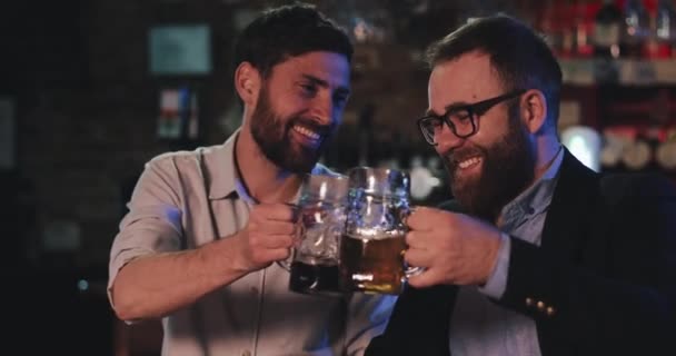 Londres Reino Unido - 14 de abril de 2019: Vista de cerca de los hombres sonrientes animando pintas de vidrio mientras se divierten en el pub. Amigos despreocupados disfrutan bebiendo cerveza fría y charlando en el bar. Concepto de ocio . — Vídeo de stock