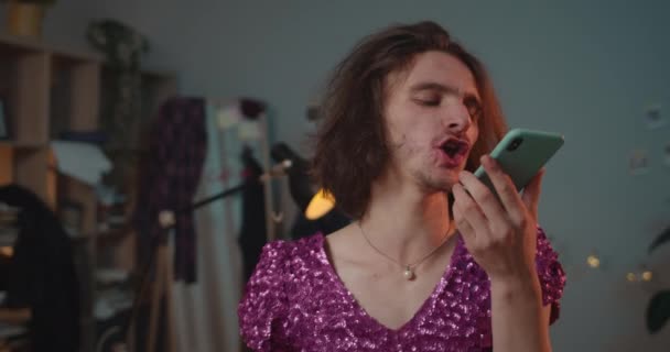 Närbild av ung transsexuell man i peruk gör arg röst budskap till sin pojkvän. Fyllda transpersoner som använder smartphone och skriker när de står hemma i moderiktig klänning. — Stockvideo
