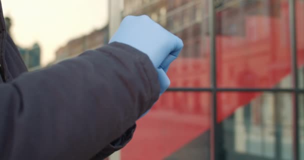 Close up άποψη των χεριών που φορούν ιατρικά γάντια λατέξ κύλιση σύγχρονη οθόνη smartphone. Έννοια της ζωής για την υγεία και την ασφάλεια, coronavirus, προστασία του ιού, πανδημία στον κόσμο. Εξωτερικές πόρτες. — Αρχείο Βίντεο