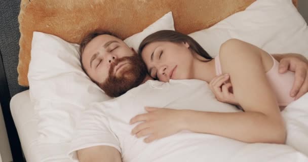Χαριτωμένο ζευγάρι αγκαλιά μαζί στο κρεβάτι, ενώ κοιμάται νωρίς το πρωί. Νεαρός άντρας και γυναίκα ξαπλωμένοι στο κρεβάτι, να ονειρεύονται αγκαλιασμένοι. Έννοια της σχέσης. — Αρχείο Βίντεο