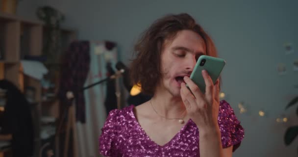 Close up view of angry transgender man in shouting fuck you into smartphone loudspeacker. Drunky transgender yelling on friend while standing at home in fashionable dress with sequins. — Αρχείο Βίντεο