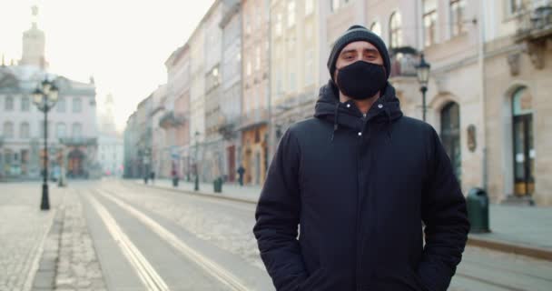 Portrait of man in black protective cotton mask standing at empty street of old europian city. Concept of health and safety life, coronavirus, virus protection, pandemic in world. — Stock Video