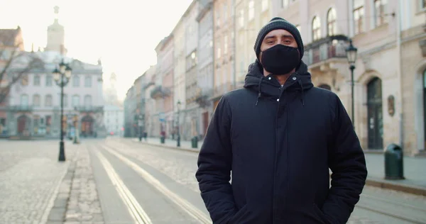Potret manusia bertopeng kapas hitam pelindung berdiri di jalan kosong kota tua europi. Konsep kesehatan dan keselamatan, coronavirus, perlindungan virus, pandemi di dunia. Stok Foto Bebas Royalti