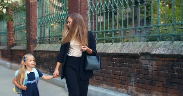 Hermosa joven madre y su pequeña hija tomados de la mano y caminando. Mujer atractiva hablando con su hijo mientras van de camino a la escuela. Concepto de relaciones familiares . — Vídeos de Stock