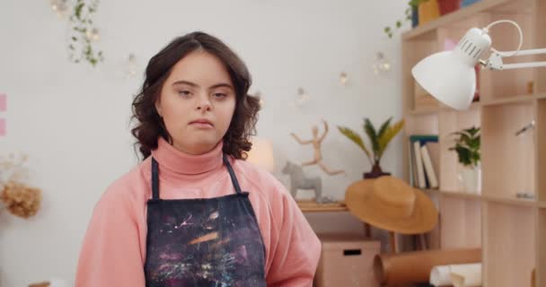 Portret van een leuk mooi meisje met down syndromee in een schort en kijkend naar de camera. Mooie vrouwelijke tiener poseren om camera terwijl ze in haar kamer. Begrip "mens". — Stockvideo