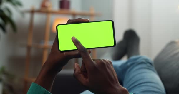 Man bläddra smartphone mocka upp skärmen medan du håller den i horisontellt liggande läge. Killen tittar på video blogg medan du ligger på soffan. Begreppet kromnyckel och grön skärm . — Stockvideo