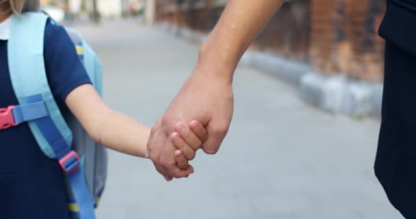 Close-up zicht van moeder en dochter lopen hand in hand op straat. Mam brengt haar basiskind naar school. Begrip gezinsrelatie. — Stockvideo
