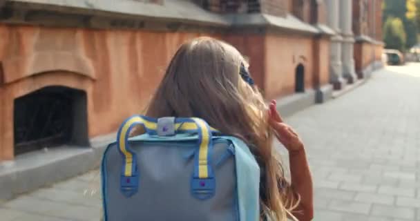 Una foto de seguimiento de una niña corriendo al edificio de la escuela. Vista trasera de una niña pequeña con una bolsa en la espalda apresurándose en las lecciones. Concepto de niños y educación. Al aire libre . — Vídeos de Stock