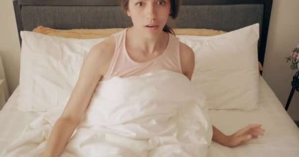 Belle femme qui tient sa tête avec les deux mains pendant qu'elle dort et qui retombe sur son lit. Fille millénaire regardant inquiet tout en réalisant réveil tardif pour le travail. Concept de style de vie . — Video