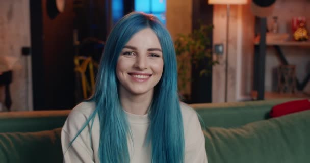 Portret van vrolijke mooie vrouw met blauw haar kijkend naar de camera en glimlachend. Modern millennial meisje zitten op de bank en poseren thuis. Concept van mensen en emoties. — Stockvideo