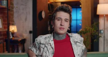 Dövmeli ve piercingli genç adamın ciddi bir yüzle kameraya bakışını yakından izle. Kanepede oturan modern milenyum adamının portresi. Gayri resmi insan kavramı.