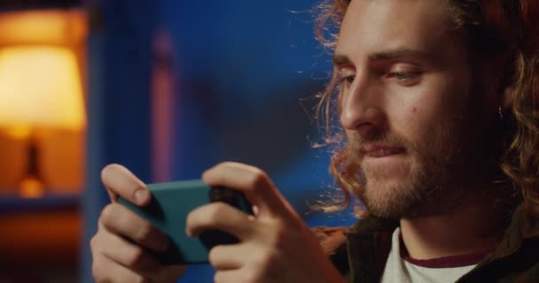 Zbliżenie przystojnego męskiego gracza trzymającego smartfona poziomo i grającego w gry online. Przycięty widok faceta patrząc na ekranie z podnieceniem, wygrywając kolejny poziom w grze. — Wideo stockowe
