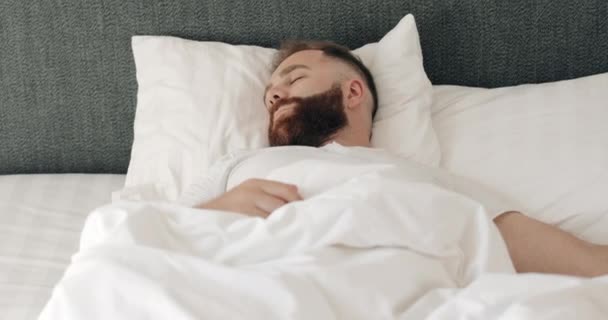 Close up view of shocked young bearded man oversleep and getting up fast while lying in bed. Красивый мужчина просыпается и кричит, осознавая, что проспал утром . — стоковое видео