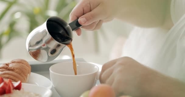 Közelről láthatjuk, ahogy a férfiak forró kávét öntenek a csészébe. Az ember az ágyban reggelizik tálcán kora reggel. A boldog életmód fogalma. — Stock videók