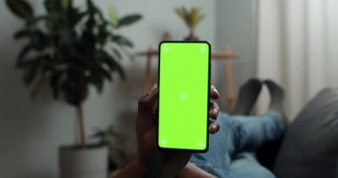 Kanepede yatarken elinde akıllı telefon tutan bir adamın görüntüsünü kapat. Afro-Amerikalı adam evde dinlenirken telefon kullanıyor. Krom anahtar ve yeşil ekran kavramı.