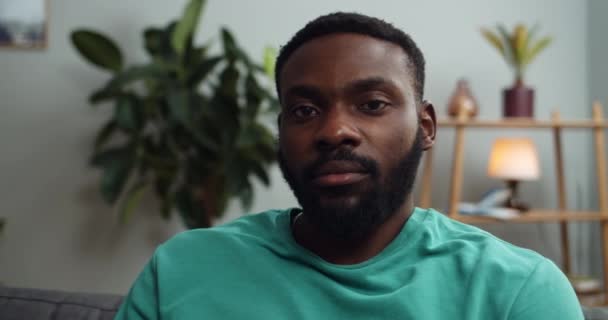 Vue rapprochée de l'homme sérieux assis sur le canapé et posant devant la caméra. Portrait d'un beau afro-américain regardant caméra. Concept de personnes et d'émotions. Accueil arrière-plan . — Video