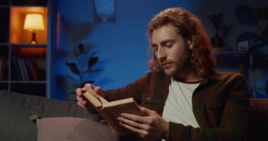 Akıllı genç adam elinde kitapla kanepede oturuyor ve gecenin geç saatlerinde uykulu görünüyor. Yakışıklı hippi evde ilginç hikayeler okurken esniyor ve yorgun hissediyor. Boş zaman kavramı..