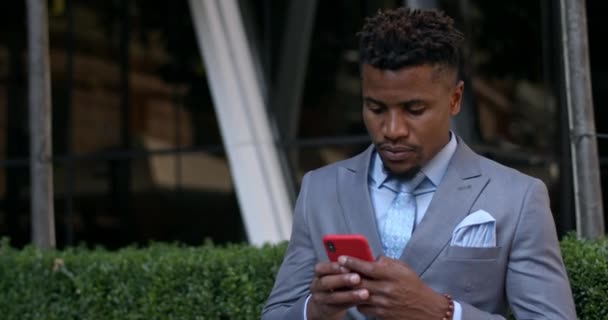 Koncentrerad vuxen affärsman som använder sin moderna smartphone stående på gatan. Framgångsrik kille i 30-årsåldern bär klassisk kostym och slips ser och berörande telefonskärm. — Stockvideo