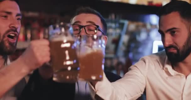 Lviv, Ucrânia - 19 de abril de 2019: Amigos alegres batendo cervejas de vidro enquanto se divertem no pub. Rapazes felizes a torcer cerveja e a comunicar enquanto relaxam depois do dia de trabalho . — Vídeo de Stock