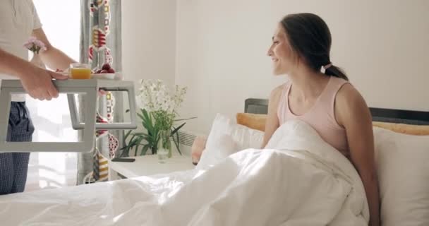 Opiekujący się przystojnym mężem przynoszący żonie śniadanie do łóżka wcześnie rano. Brodaty facet w piżamie niosący jedzenie na tacy dla swojej uroczej dziewczyny w sypialni. Pojęcie stosunku. — Wideo stockowe