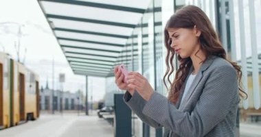 Akıllı telefonunu yatay manzara modunda tutan ve ekrana dokunan güzel bir kadın. Çekici esmer kız otobüs durağında otururken telefon ve daktilo kullanıyor..